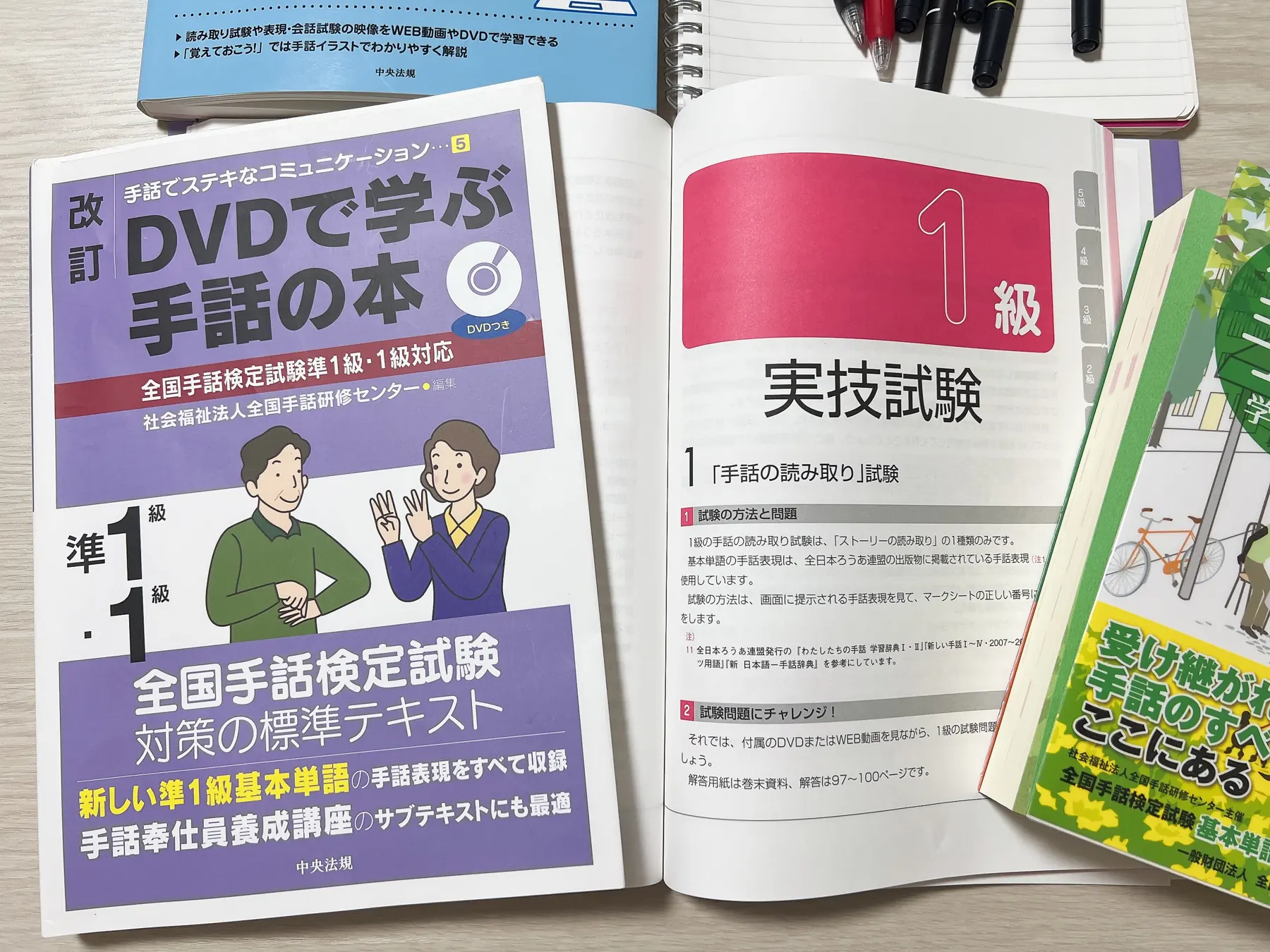 準1級・1級対応の手話テキストと、過去問題集の1級の章を机に並べた写真