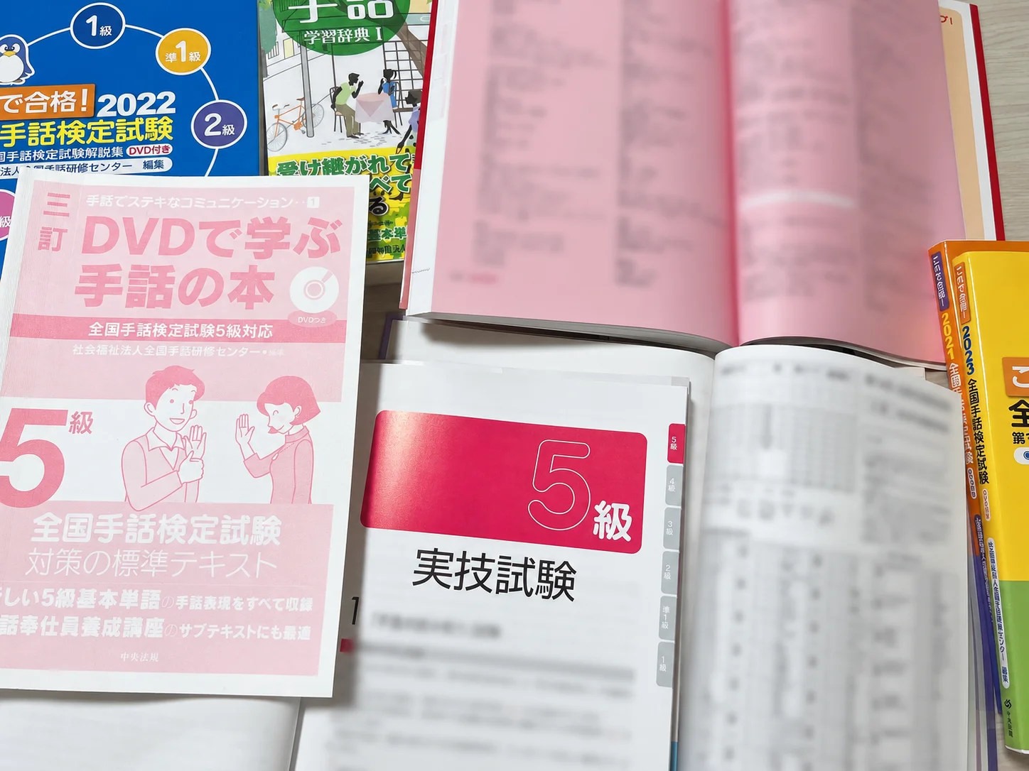 全国手話検定5級の過去問題集と標準テキストを並べ、出題内容を見比べている写真