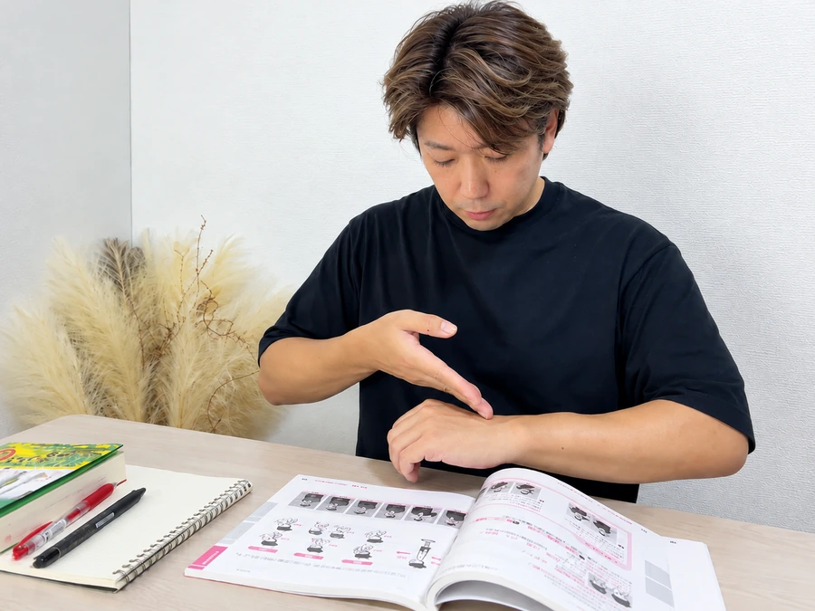 開いたテキストを机に置き、手元を見ながら手話の表現を確かめる筆者
