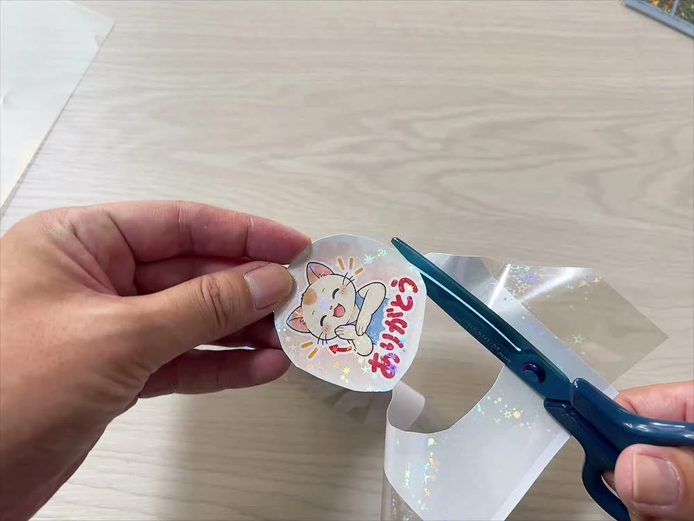 ホログラムシートを重ねた「ありがとう」の猫のキャラクターを、はさみで切り抜いている様子
