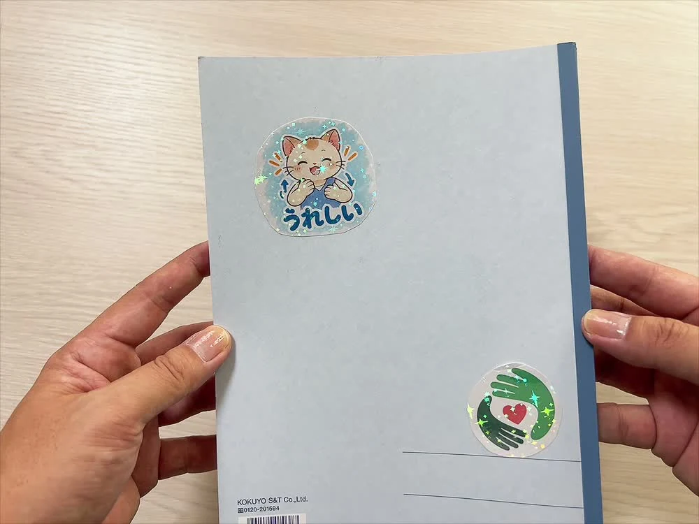 ノートの裏表紙に貼った「うれしい」の猫のキャラクターと丸い手話ライフのロゴ