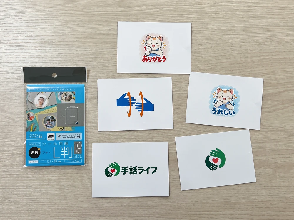 シール用紙に印刷した手話ライフのロゴ、ありがとう・うれしいの猫のキャラクター、手のイラスト