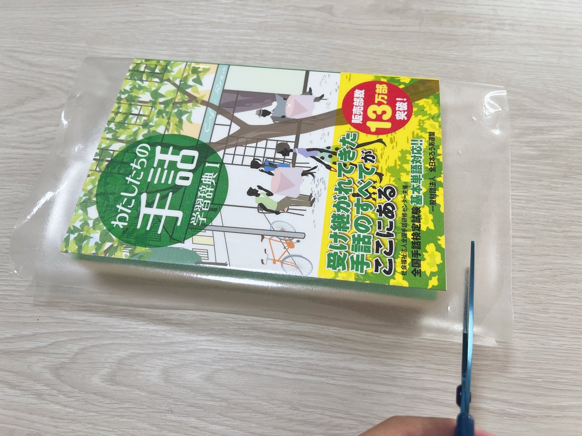 辞典の表紙に貼った保護フィルムの余分な部分をハサミで切っている様子