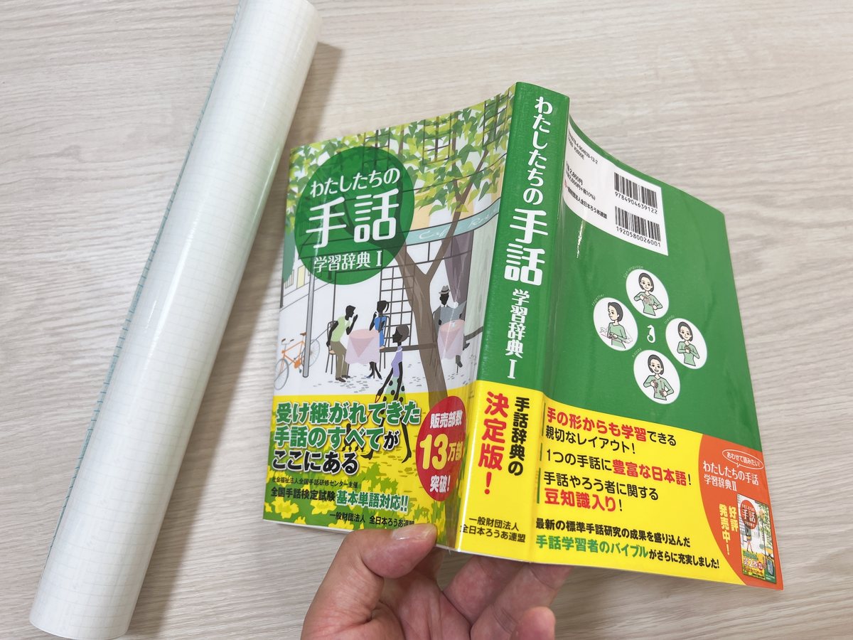 保護フィルムを貼り終えた『わたしたちの手話 学習辞典Ⅰ』の表紙、背表紙、裏表紙