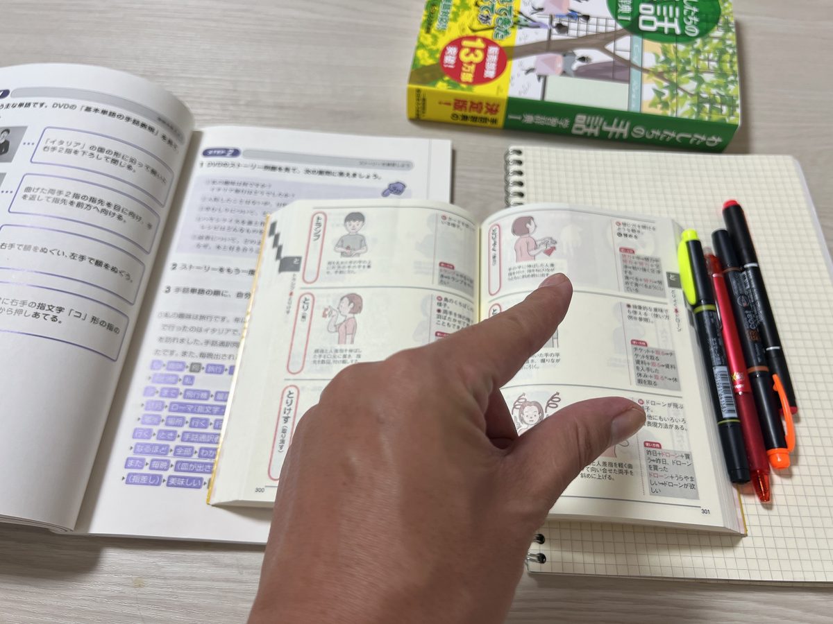 開いた教材やノートと一緒に実用手話辞典を使い、手の形を確かめている様子